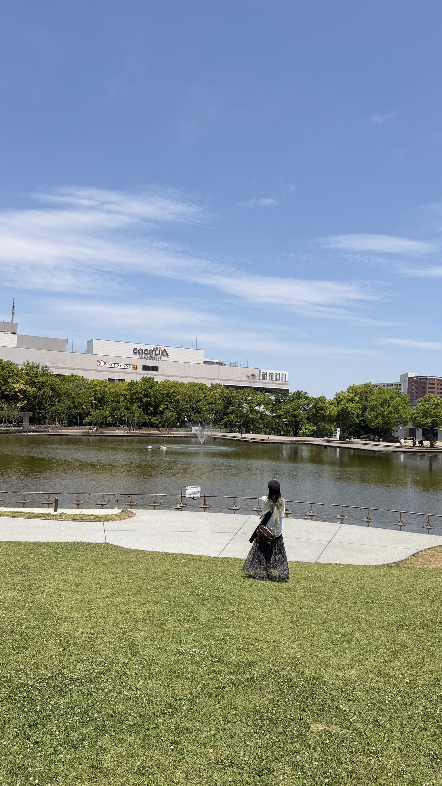 青空と池の前に立つ女性